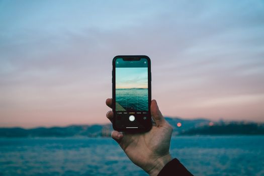 A hand holds a smartphone at sunset, capturing the Bosphorus view in Istanbul.